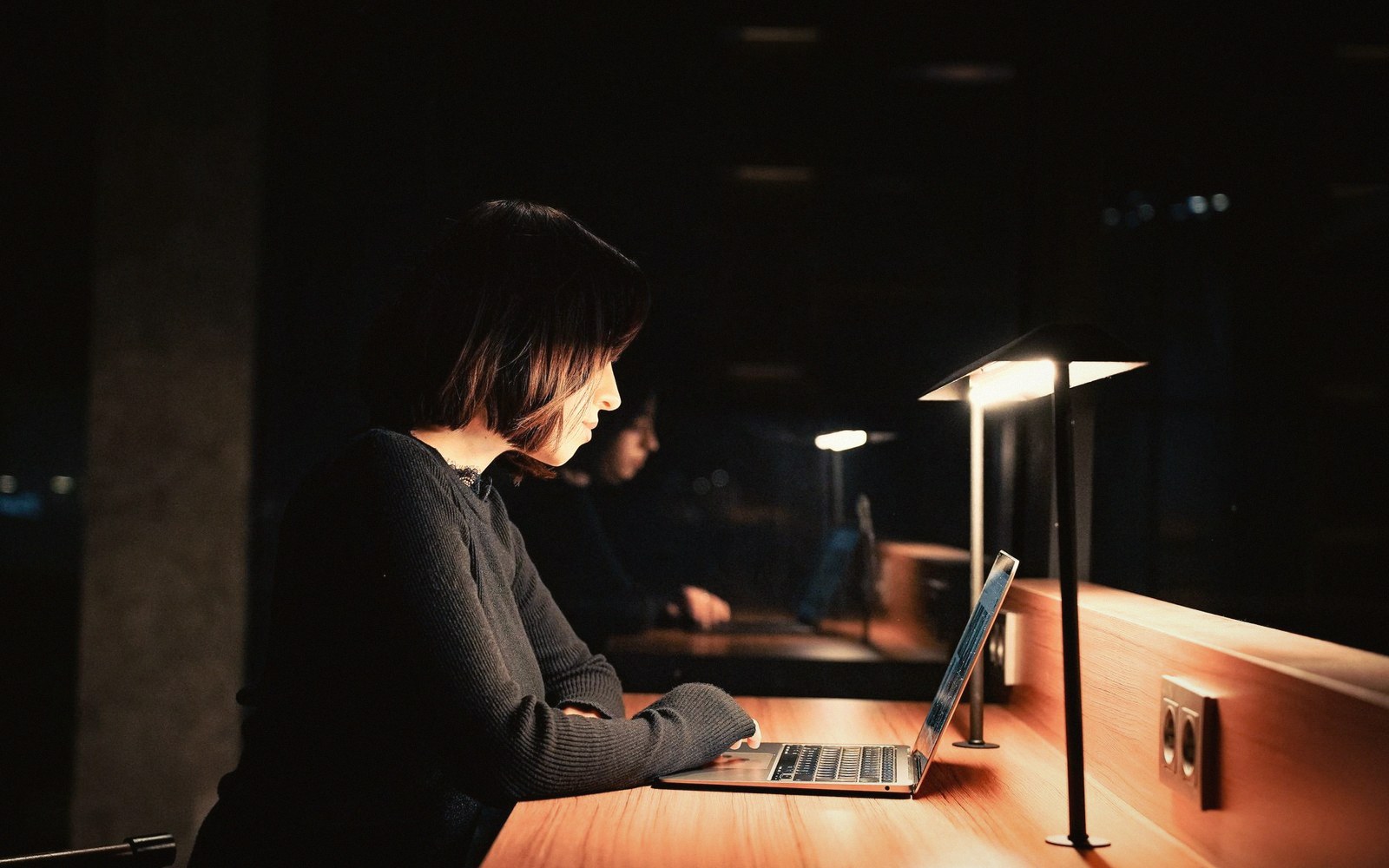 A woman working at a lamp-lit desk in a dark room